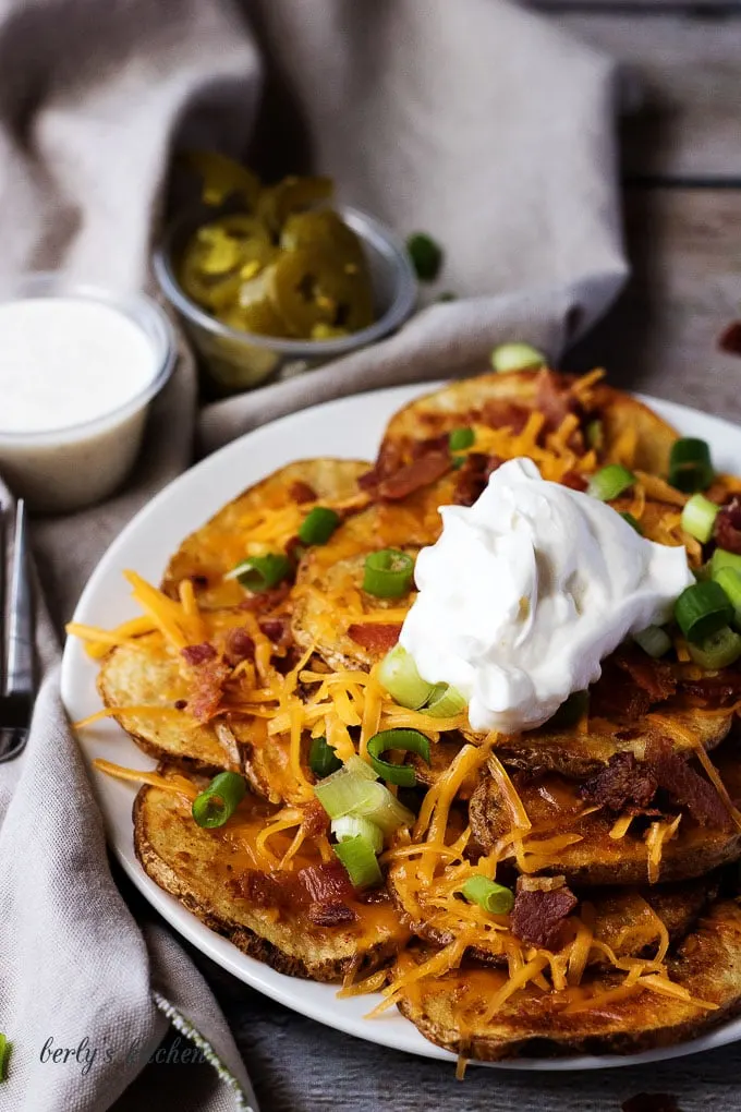 Plate of loaded potato nacho fries with cup of jalapenos in the background.