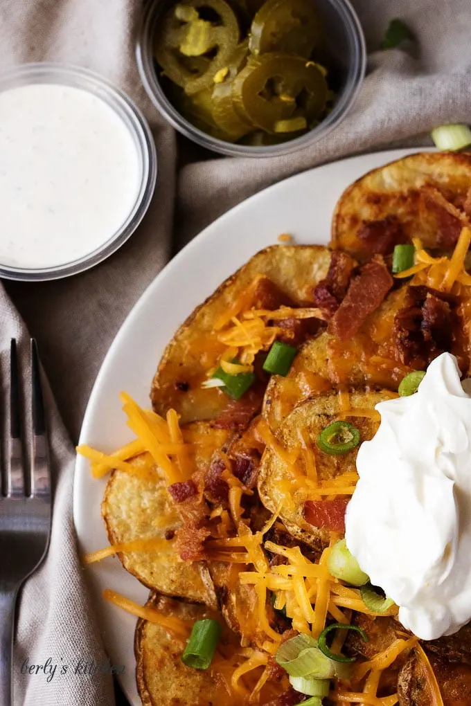 Close up of loaded potato nachos on a white plate.