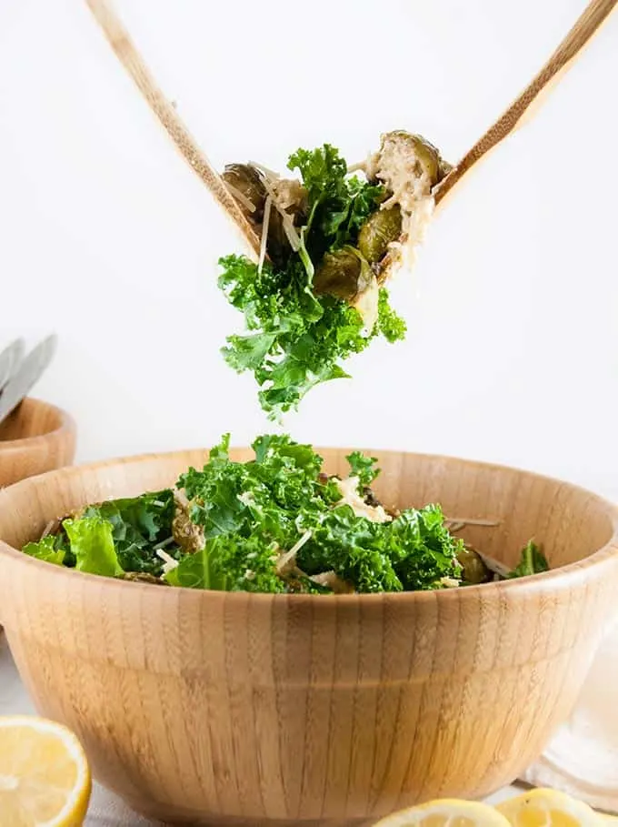 Brussels sprouts salad being tossed with wooden spoons.