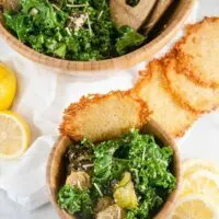 Top down view of a bowl of caesar salad with roasted brussel sprouts next to fresh lemons and parmesan crisps.