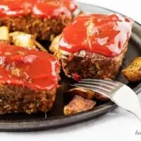 Mini meatloaves topped with ketchup next to two forks.