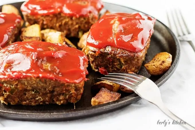 Mini meatloaves topped with ketchup next to two forks.