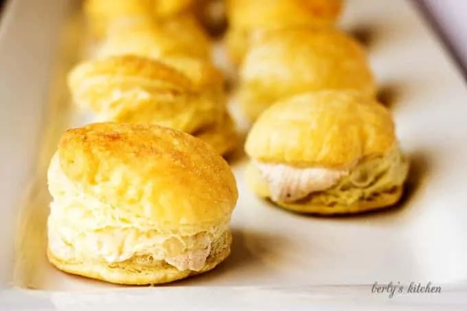 Rows of cream puffs stuffed with pumpkin spiced cream cheese on a white plate.