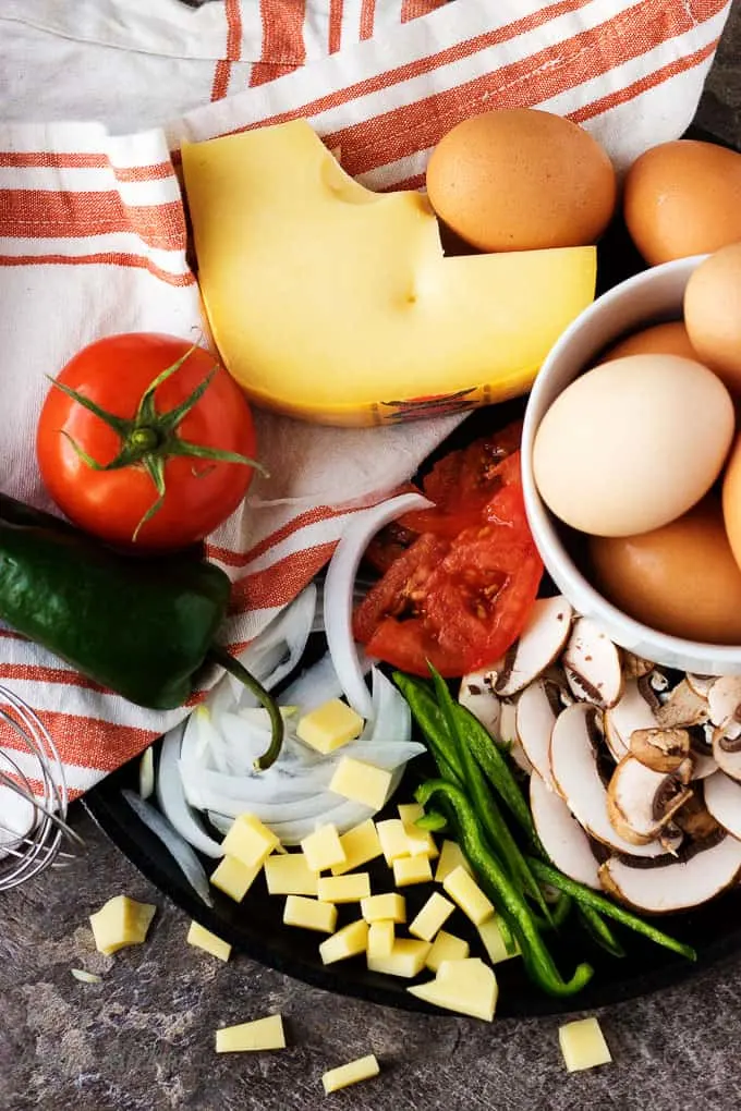 The white bowl filled with eggs, surrounded by ingredients, and resting on a flat-iron griddle.