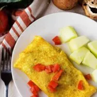 A top-down view of the dish with the omelet and melon chunks. Omelet is garnished with diced tomato.