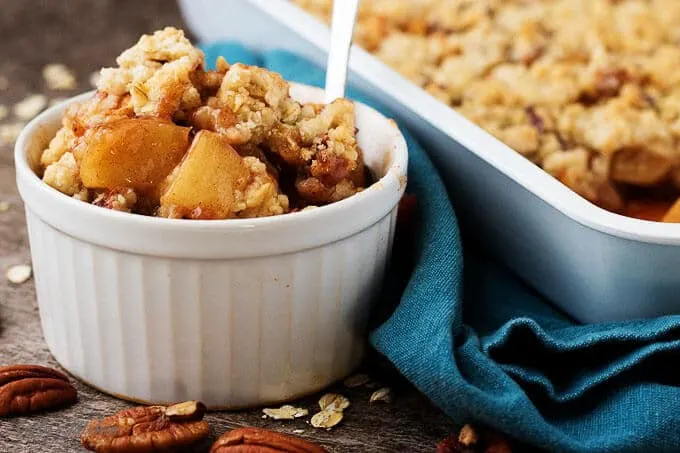 Side view of the finished apple crisp in a bowl next to the baking dish.