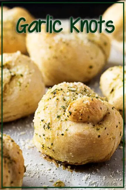 The finished garlic knots, topped with garlic butter and parmesan on a sheet pan.