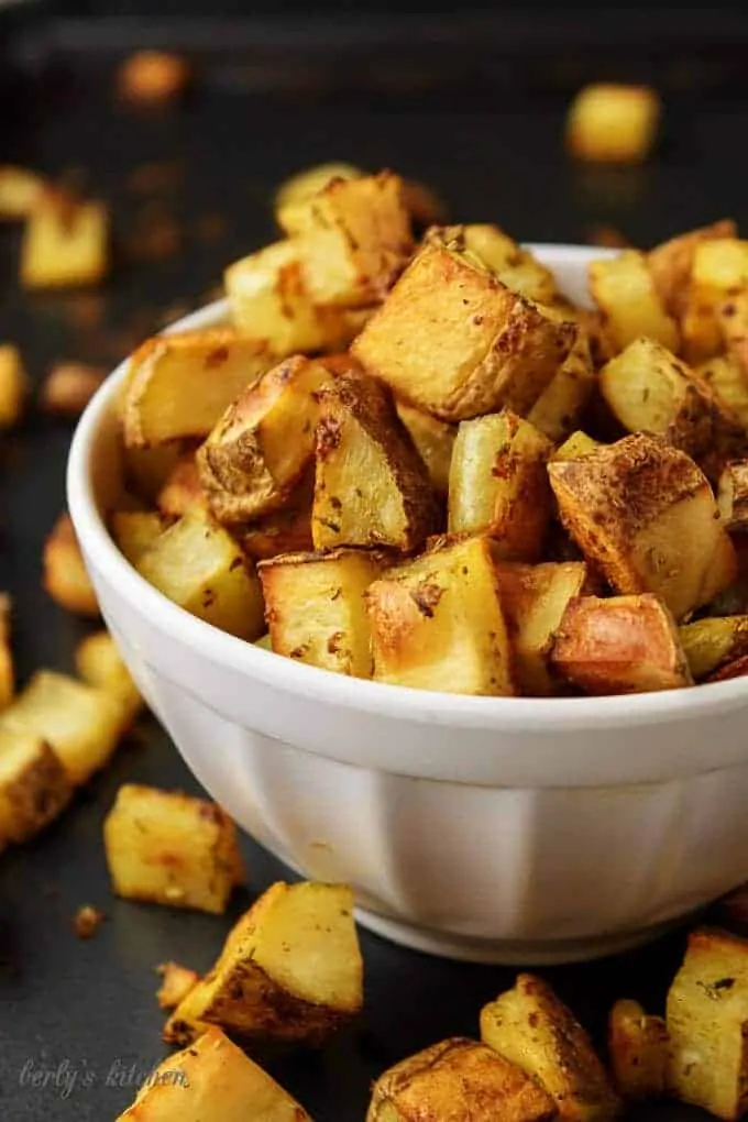 Oven-baked home fries in a white bowl on a sheet pan.