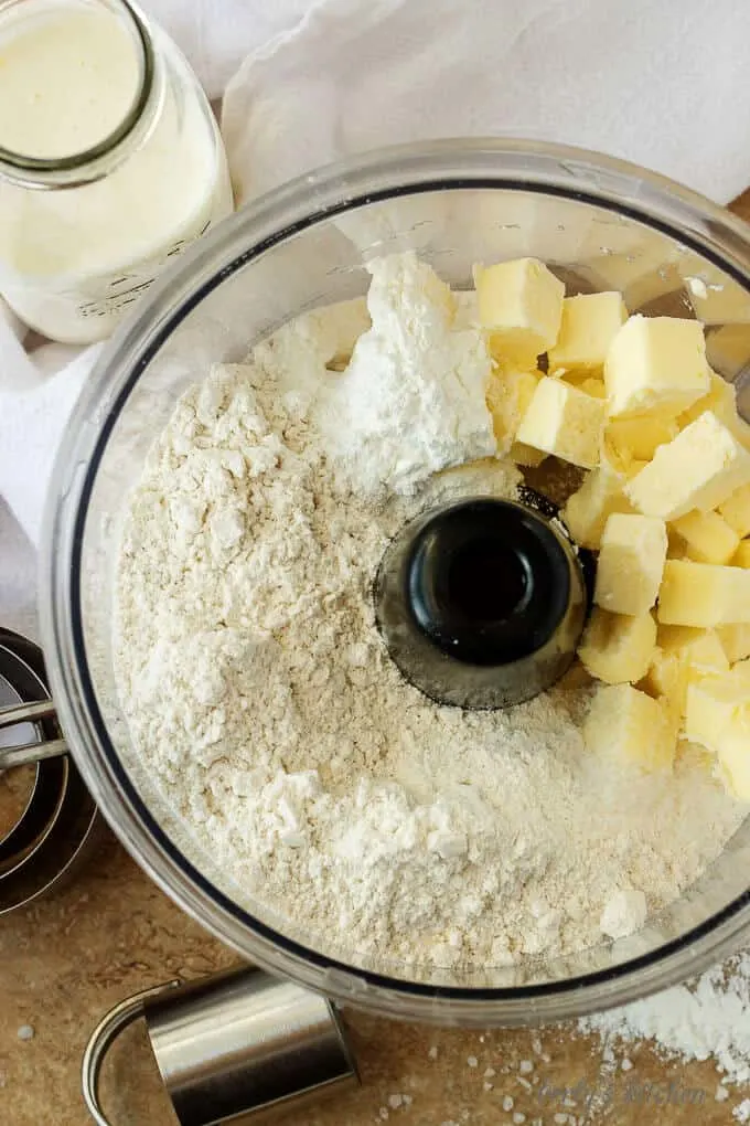 Flour, baking powder, salt, and butter needed for homemade buttermilk biscuits in a food processor.