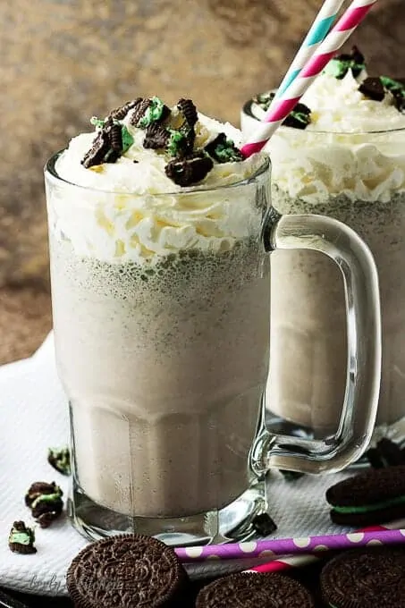 Two oreo milkshakes in chilled mugs with whipped cream and cookies toppings.