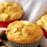 The apple cinnamon muffins in red and gray liners setting on a table.