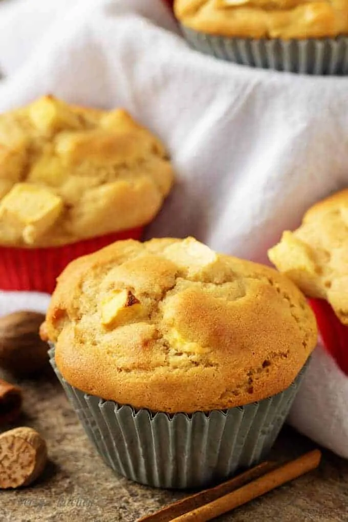 The apple cinnamon muffins in red and gray liners setting on a table.