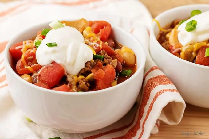 The three bean chili in a white bowl, topped with green onions and sour cream.