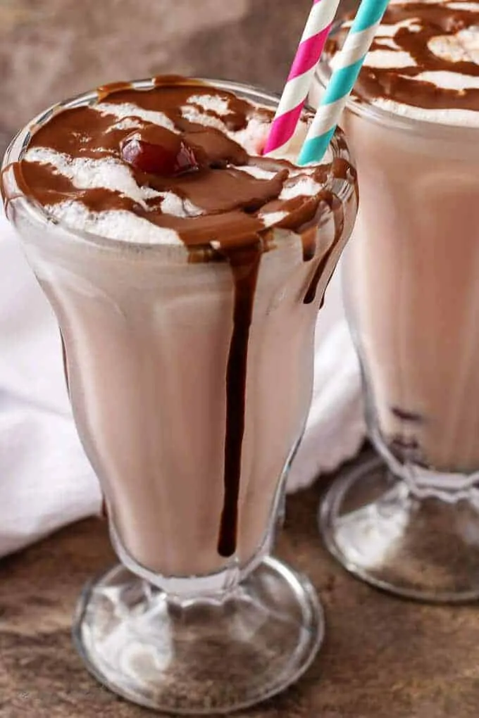 A final shot of the finished chocolate covered cherry milkshakes in glasses with straws and smothered with chocolate sauce.