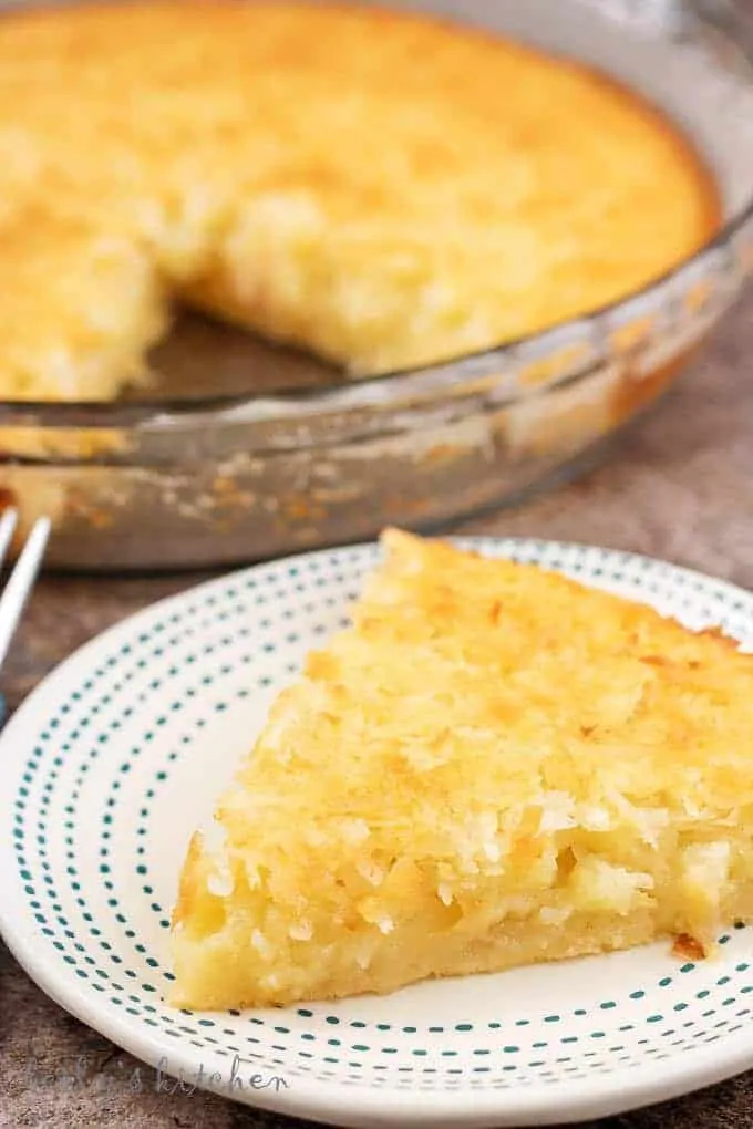 Close up photo of a slice of coconut custard pie with a pie dish in the background.