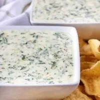 Front view of hot spinach dip in white bowls surrounded by chips.