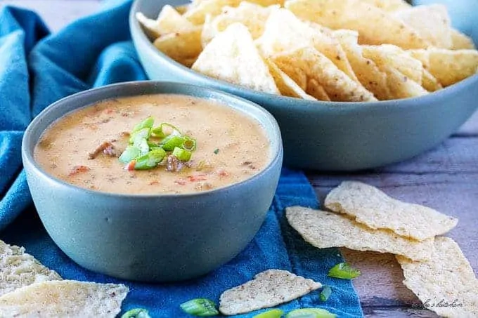 Bowl of hamburger dip next to a bowl of tortilla chips and scattered chips.