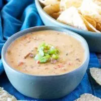 Hamburger dip in a blue bowl next to tortilla chips and green onions.