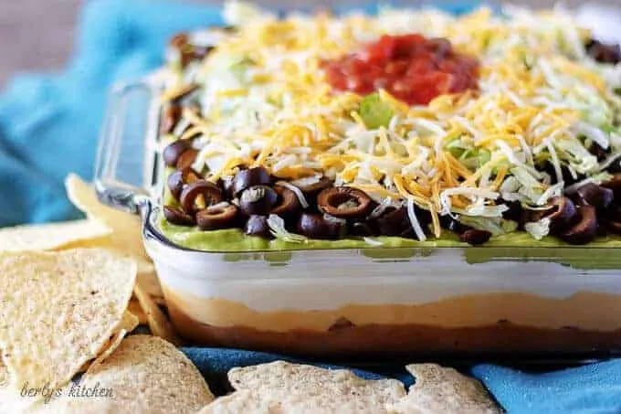 7 layer dip topped with salsa, in a large casserole dish on a blue towel.