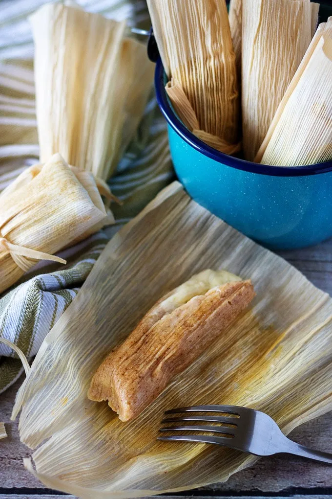 Open tamale in a corn husk next to more tamales in a blue bucket.