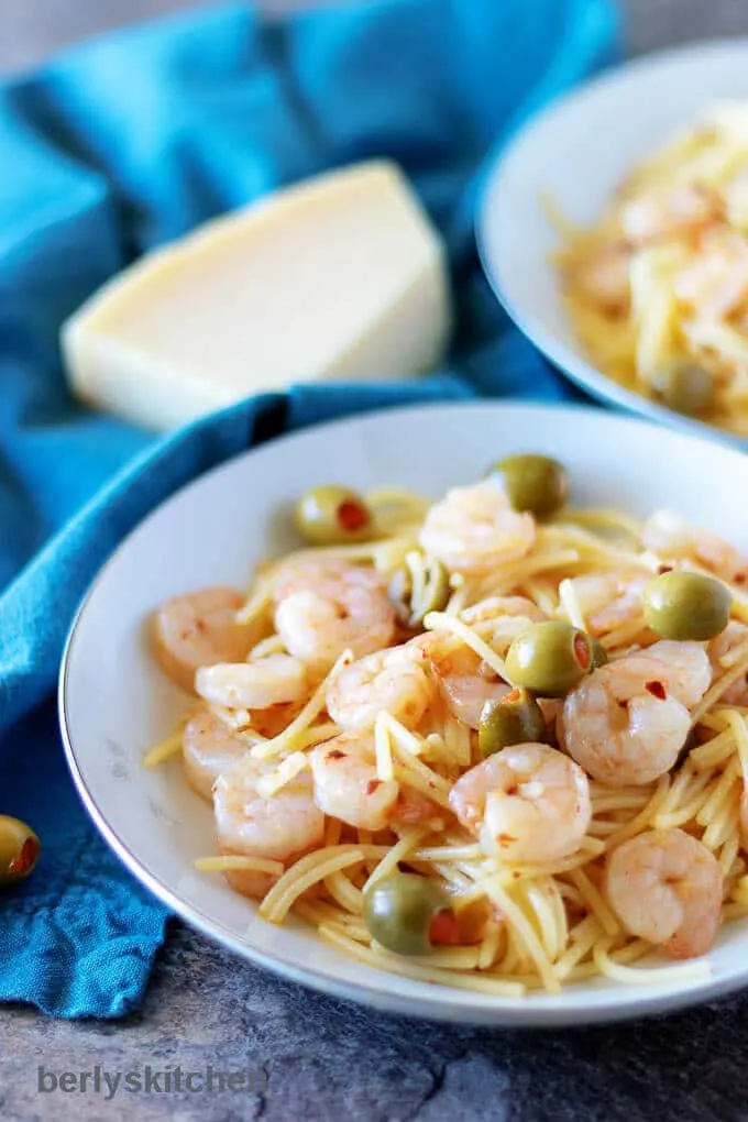 The finished shrimp and pasta garnished with olives served in white pasta bowls.