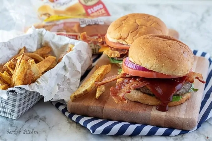 The finished bacon cheeseburgers on a cutting board, served with fries and bbq sauce.