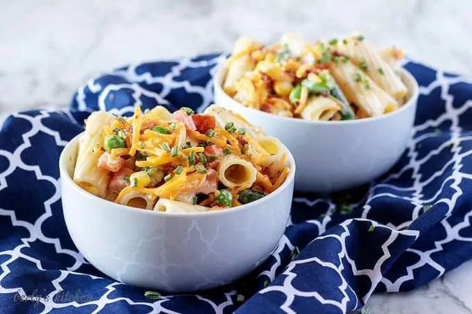 Two bowls of cold pasta salad sitting on a blue designer towel and garnished with extra cheddar cheese.