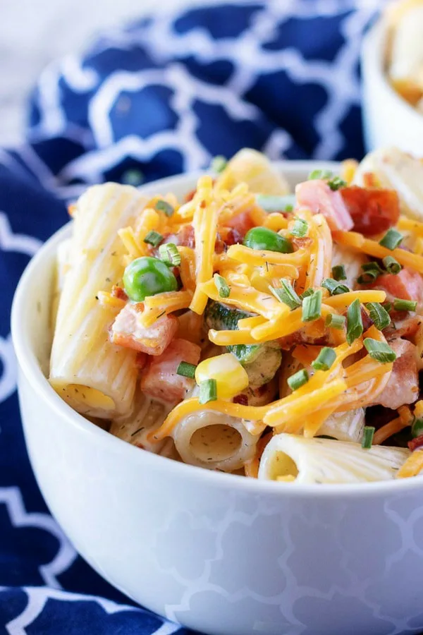 A close-up view of the cold pasta salad with vegetables garnished with cheddar cheese.