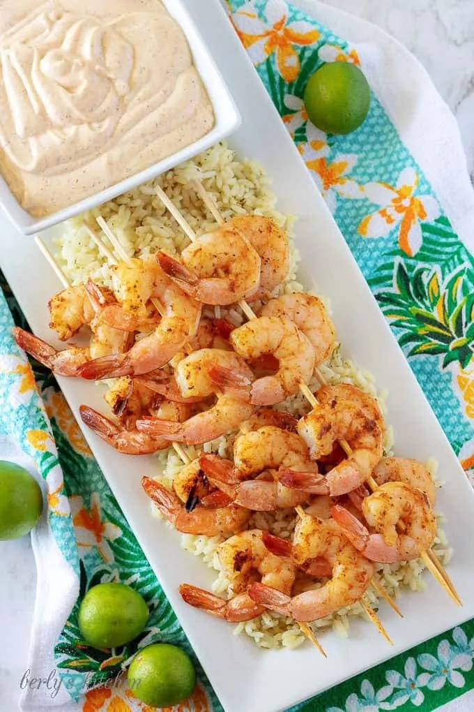 An aerial picture of the grilled shrimp skewers, over rice, with a square bowl of key lime aioli.