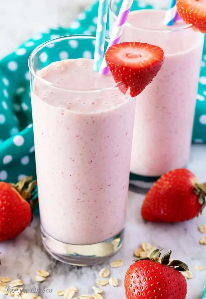 The finished strawberry banana smoothies in glasses with colorful straws and garnished with fresh strawberries.