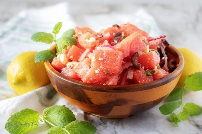 A small wooden bowl of watermelon salad, topped with fresh mint and crumbled feta cheese.