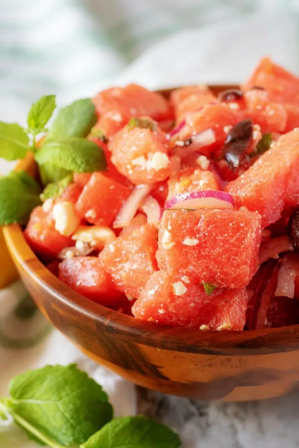 A close-up picture of the finished watermelon salad in a wooden serving bowl, garnished with mint.