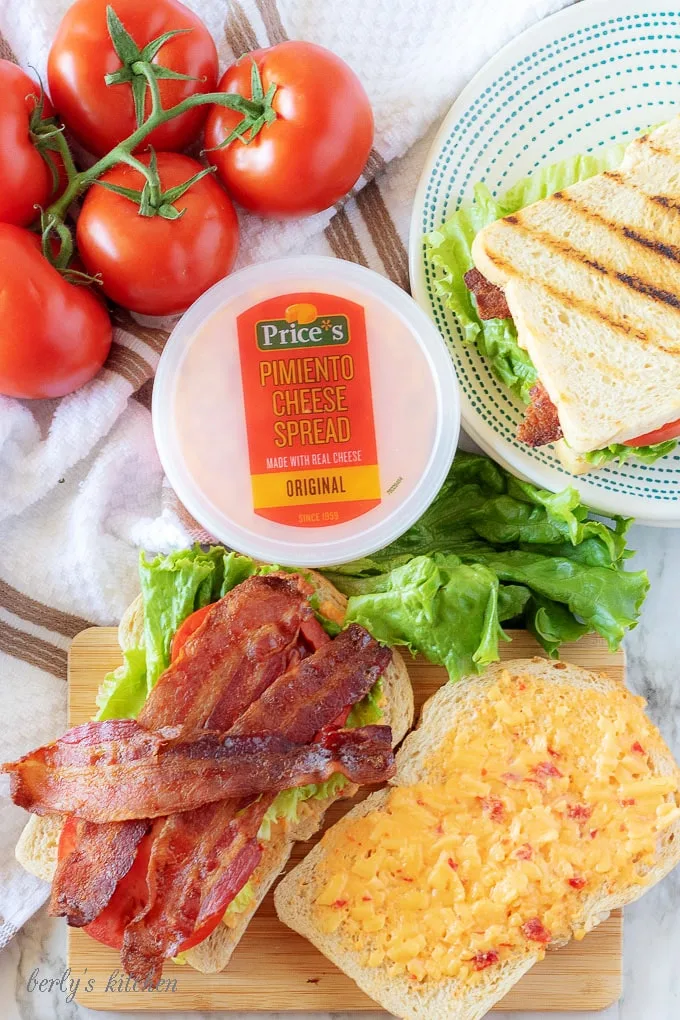 A process shot showing how to assemble the pimento cheese sandwich, starting with bread, cheese spread, lettuce, tomato, bacon, spread, then bread again.