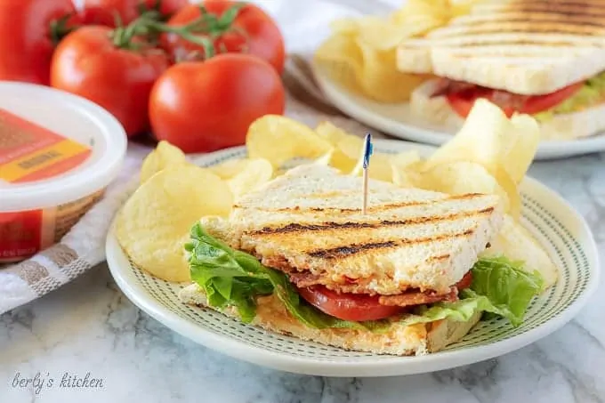 One half of the finished pimento cheese sandwich on grilled sourdough served with potato chips on white plate.