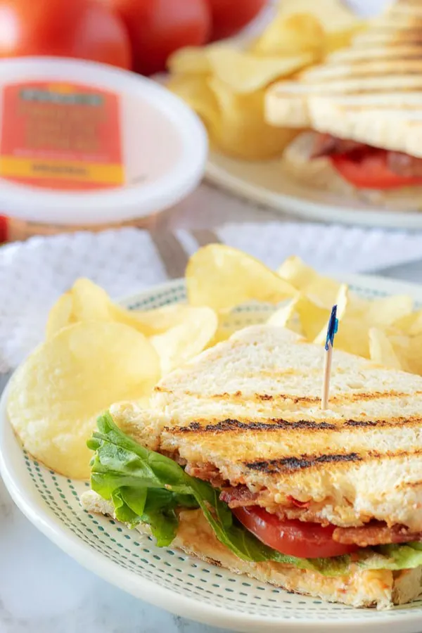 A finished half of a pimento cheese sandwich on a plate, served with crunchy potato chips.