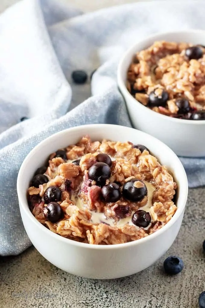 An aerial picture of the finished blueberry oatmeal garnished with fresh blueberries and heavy cream served in a white bowl.