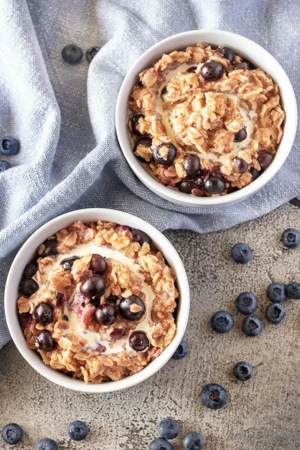 The blueberry oatmeal, top-down view, served in white bowls and garnished with fresh heavy cream and more blueberries.