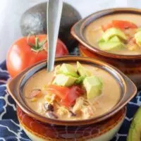 A close-up photo of the finished chicken taco soup in two earthenware bowls topped with diced tomatoes.