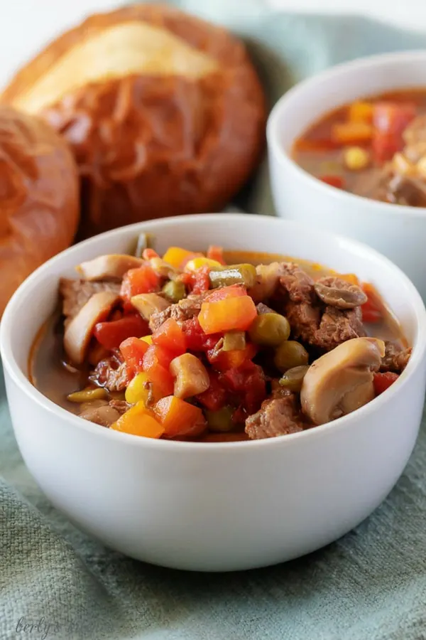 An angled photo of the finished vegetable beef soup in a whit bowl served with a pretzel roll.