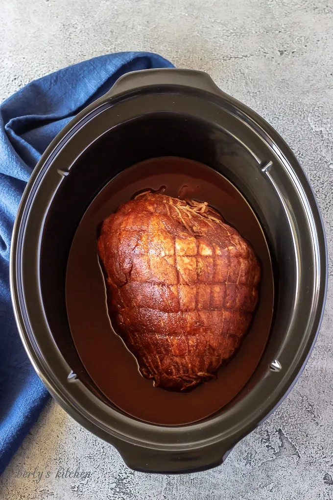 The raw pork sitting in a large slow cooker, surrounded by homemade bbq sauce.