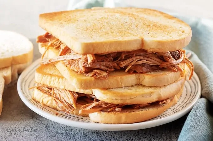 Two stacked pulled pork sandwiches, ready to be served on a white and green plate.