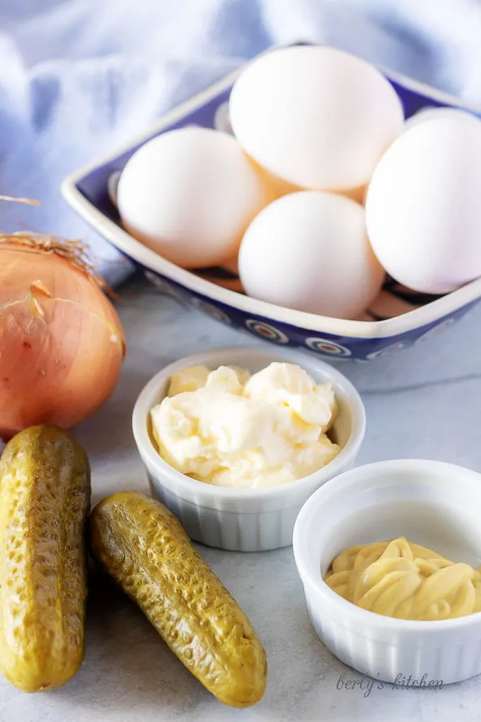 All of the easy deviled eggs ingredients like pickles, mayonnaise, mustard, and whit onion in bowl.