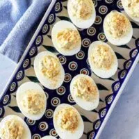 A top-down photo of the finished easy deviled eggs, garnished with paprika and sitting on a pottery serving dish.