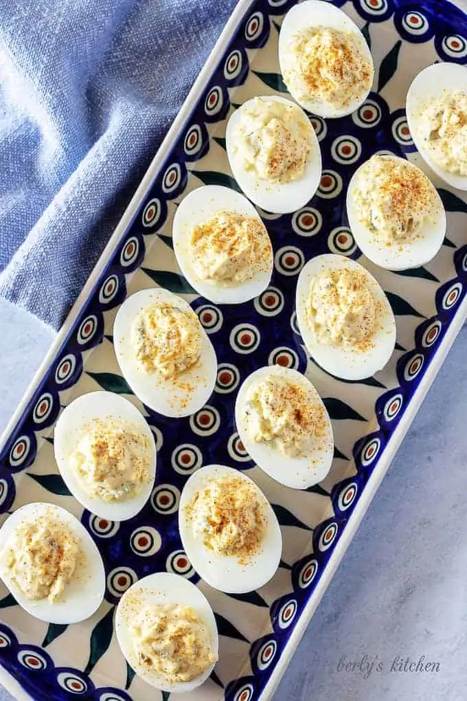 A top-down photo of the finished easy deviled eggs, garnished with paprika and sitting on a pottery serving dish.