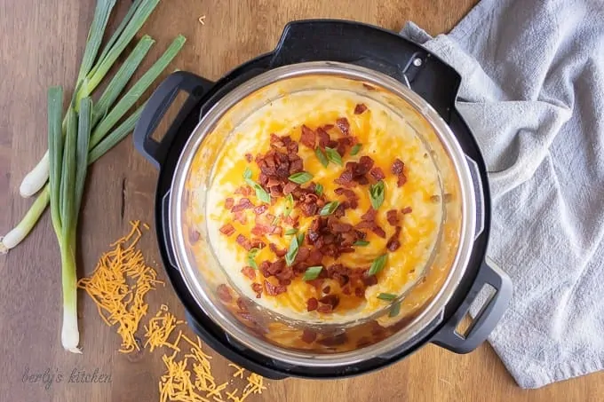 Arial view of loaded mashed potatoes in an instant pot next to shredded cheese, scallions, and a blue linen.