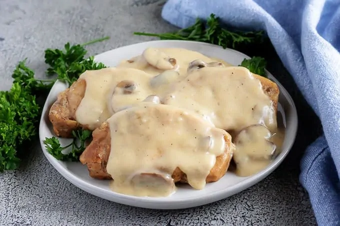 The finished instant pot pork chops covered in white mushroom gravy and garnished with fresh parsley.