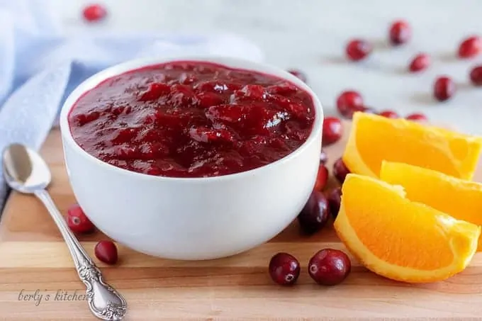 The finished orange cranberry sauce in a white bowl surrounded by fresh cranberries.