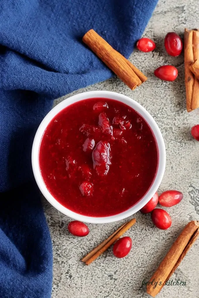 The last photo shows the finished homemade cranberry sauce in a bowl accented with cinnamon sticks.