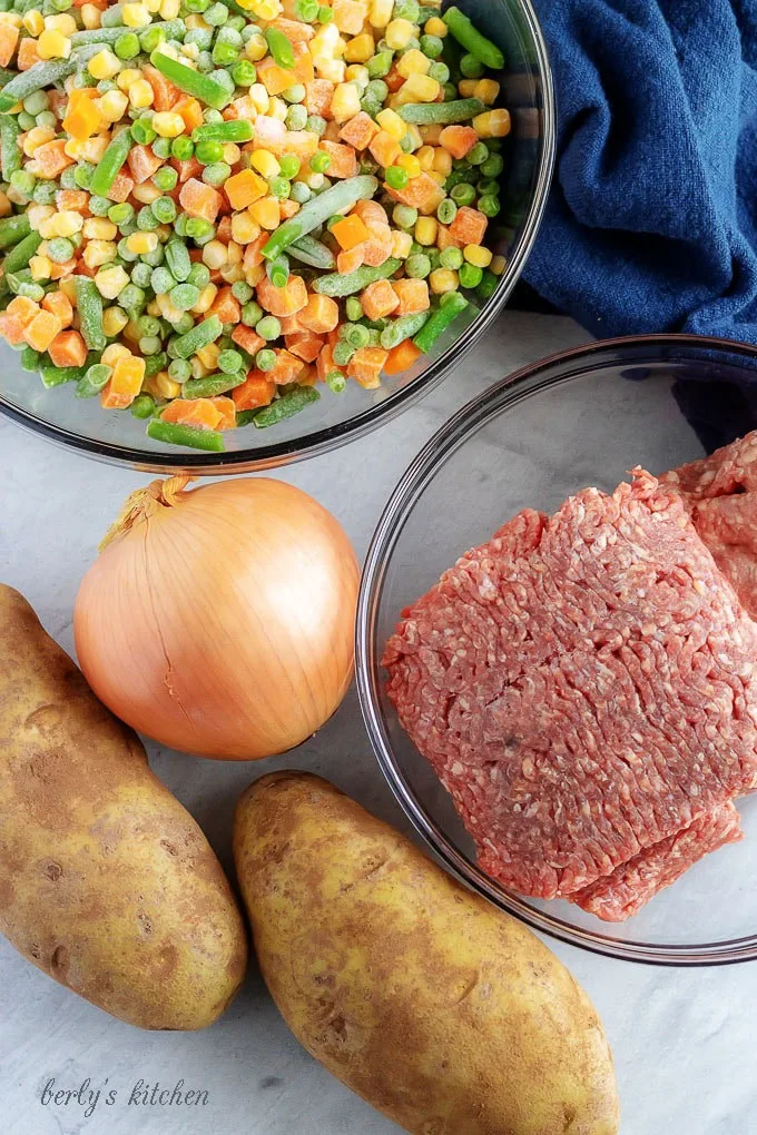 A top-down photo of the shepherd's pie ingredients, like ground beef, lamb, and frozen veggies.