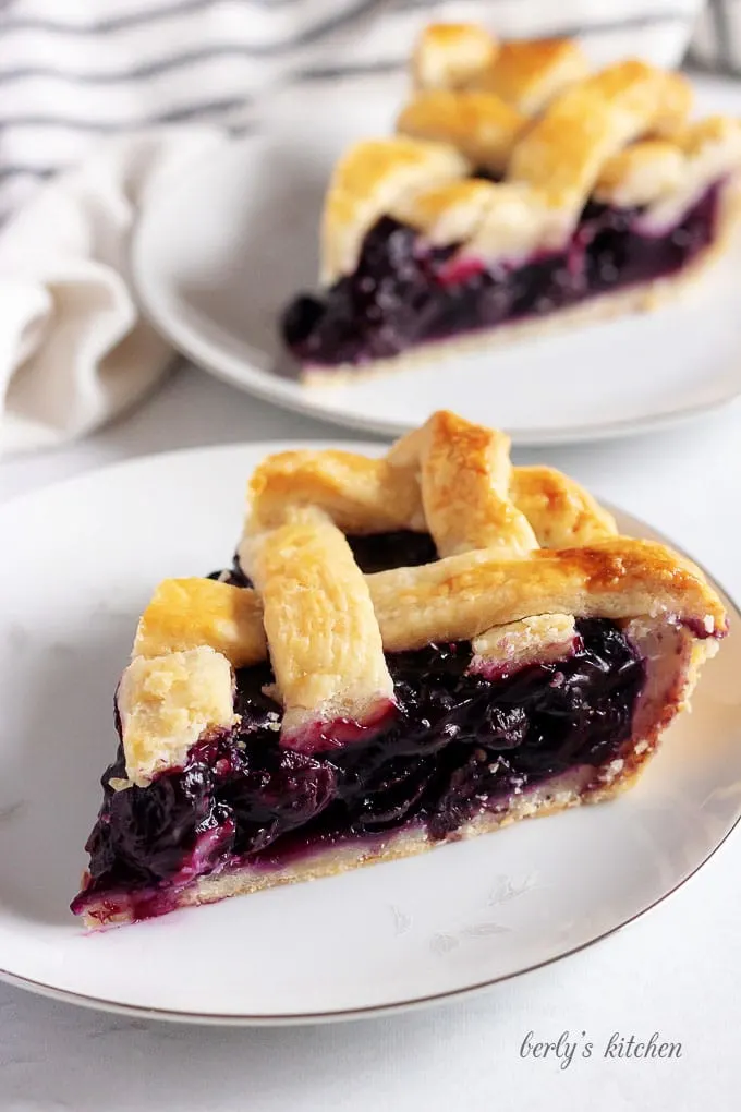 A photo showing two slices of blueberry pie on white plates.